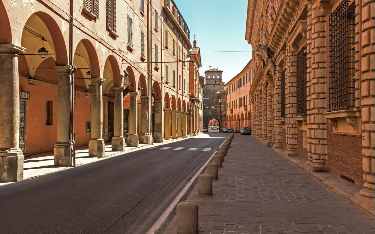 Street with historic porticoes in Bologna, Italy, part of a self-guided city exploration game.