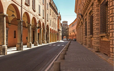 Street with historic porticoes in Bologna, Italy, part of a self-guided city exploration game.