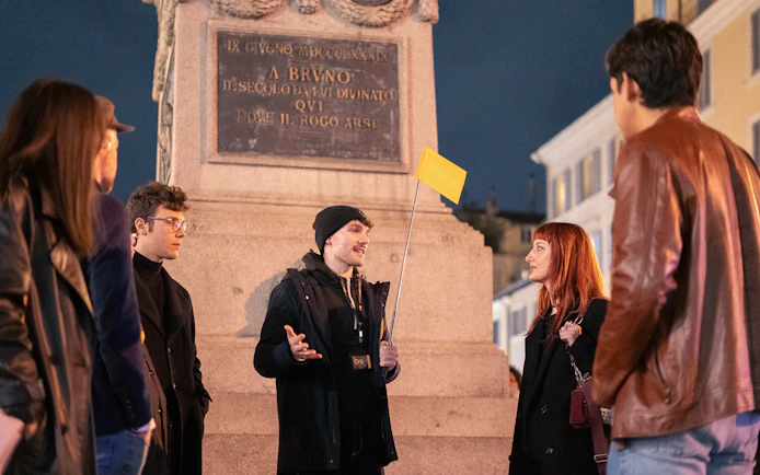 Local guide leading a haunted ghost tour at night near a monument in Rome.
