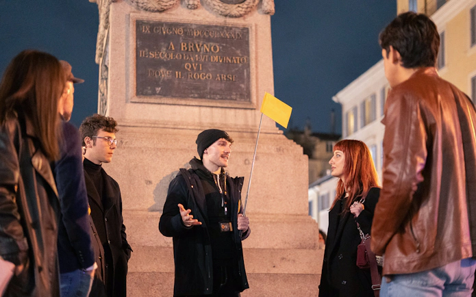 Local guide leading a haunted ghost tour at night near a monument in Rome.