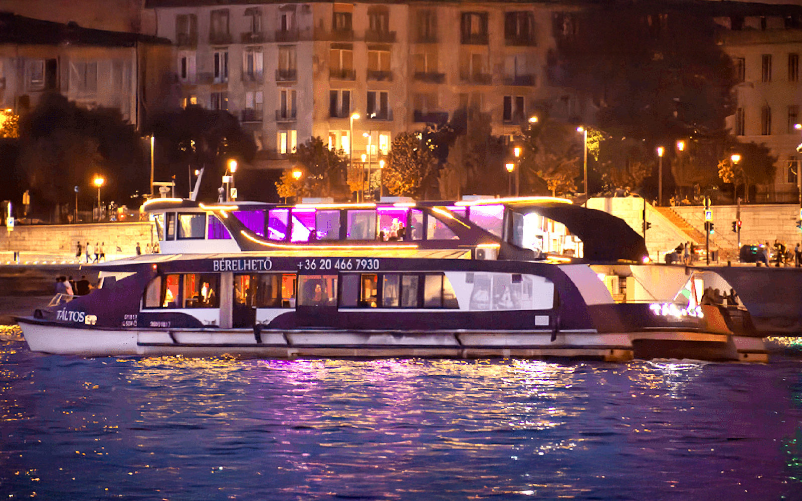 Cruise boat on the Danube River in Budapest at night with city lights in the background.