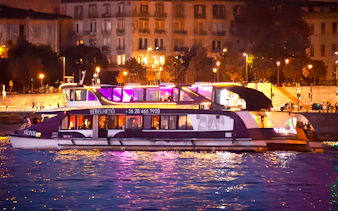 Cruise boat on the Danube River in Budapest at night with city lights in the background.