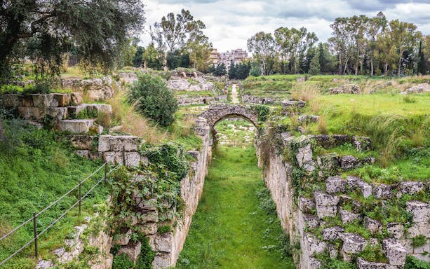 Ancient stone ruins and greenery at Neapolis Archaeological Park, Syracuse.