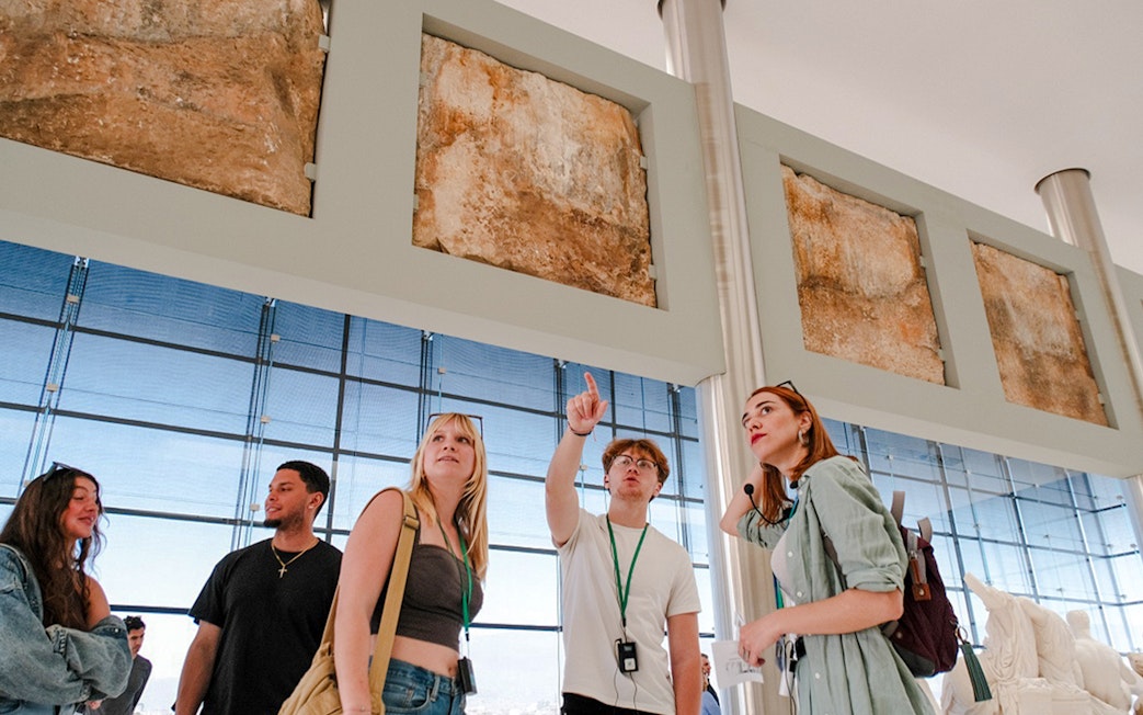 Visitors on a guided tour in Acropolis Museum examining ancient artifacts.