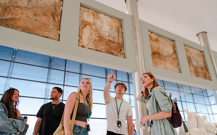 Visitors on a guided tour in Acropolis Museum examining ancient artifacts.
