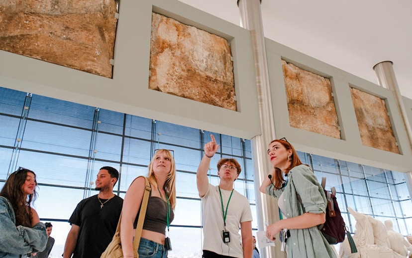 Visitors on a guided tour in Acropolis Museum examining ancient artifacts.