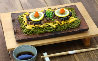 Kawara soba with green tea buckwheat noodles on a roof tile, topped with lemon and garnish.