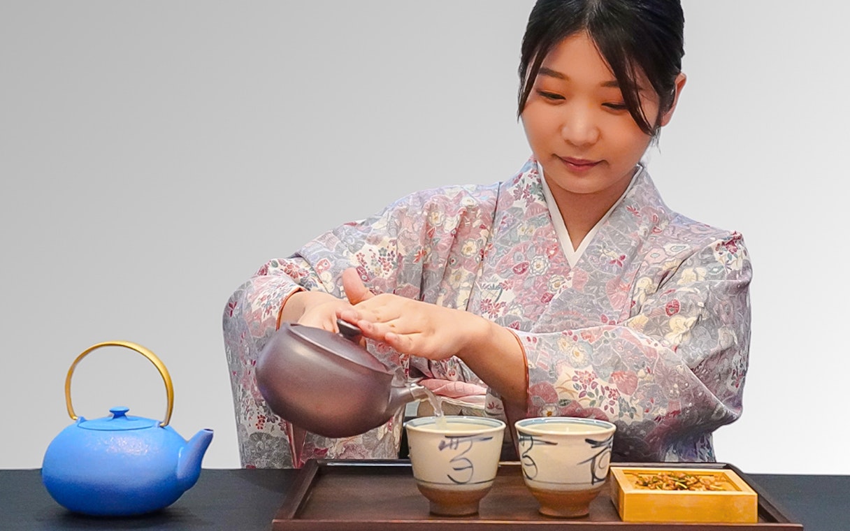 Woman in kimono pouring tea into bowls during a traditional Japanese tea ceremony.