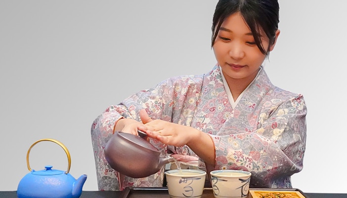 Woman in kimono pouring tea into bowls during a traditional Japanese tea ceremony.