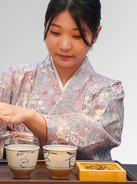 Woman in kimono pouring tea into bowls during a traditional Japanese tea ceremony.
