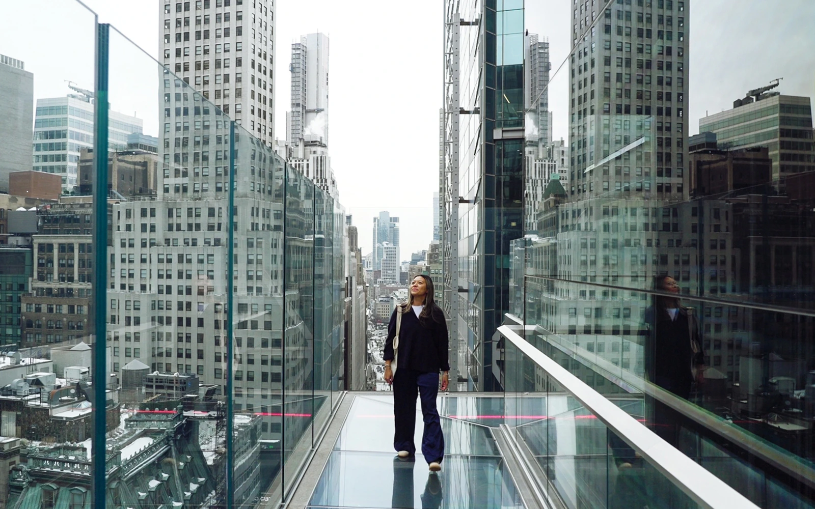 Person walking on One Times Square Skywalk with cityscape views of New York buildings.
