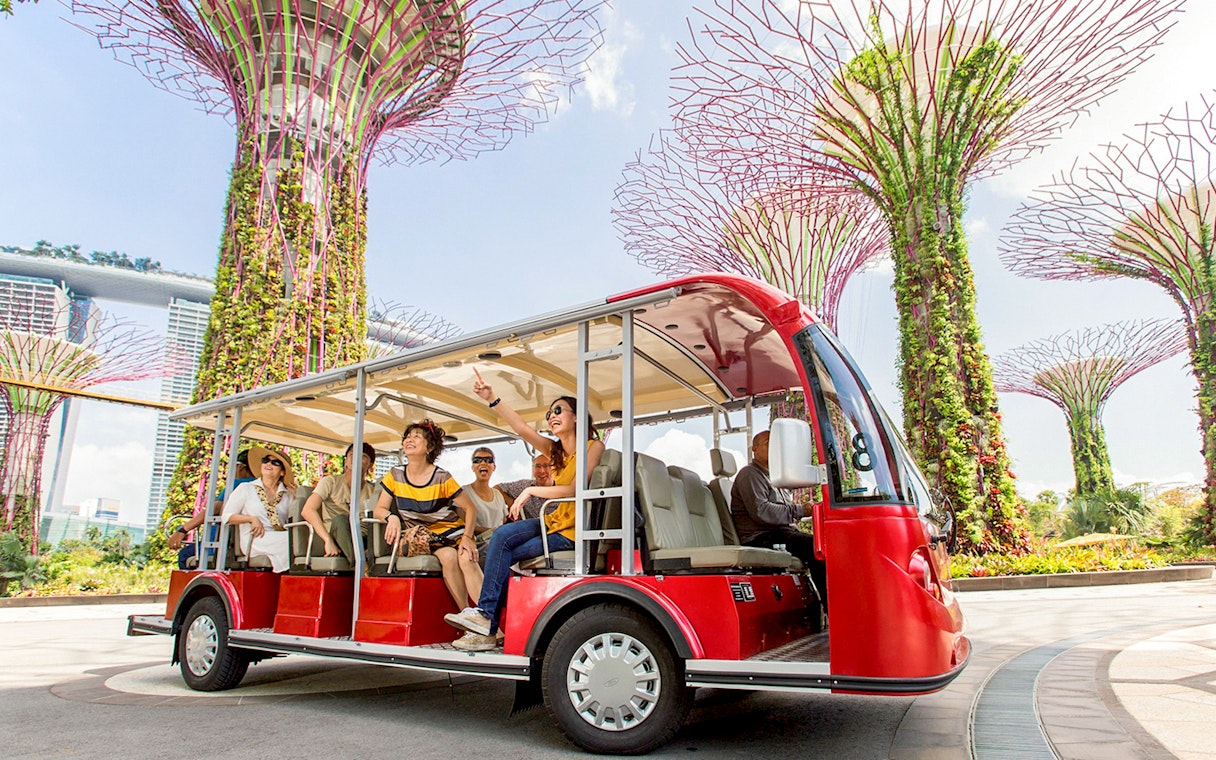 Tourists on a tram tour at Gardens by the Bay, Singapore, with Supertree Grove in view.