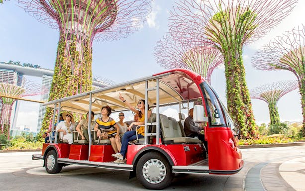 Tourists on a tram tour at Gardens by the Bay, Singapore, with Supertree Grove in view.