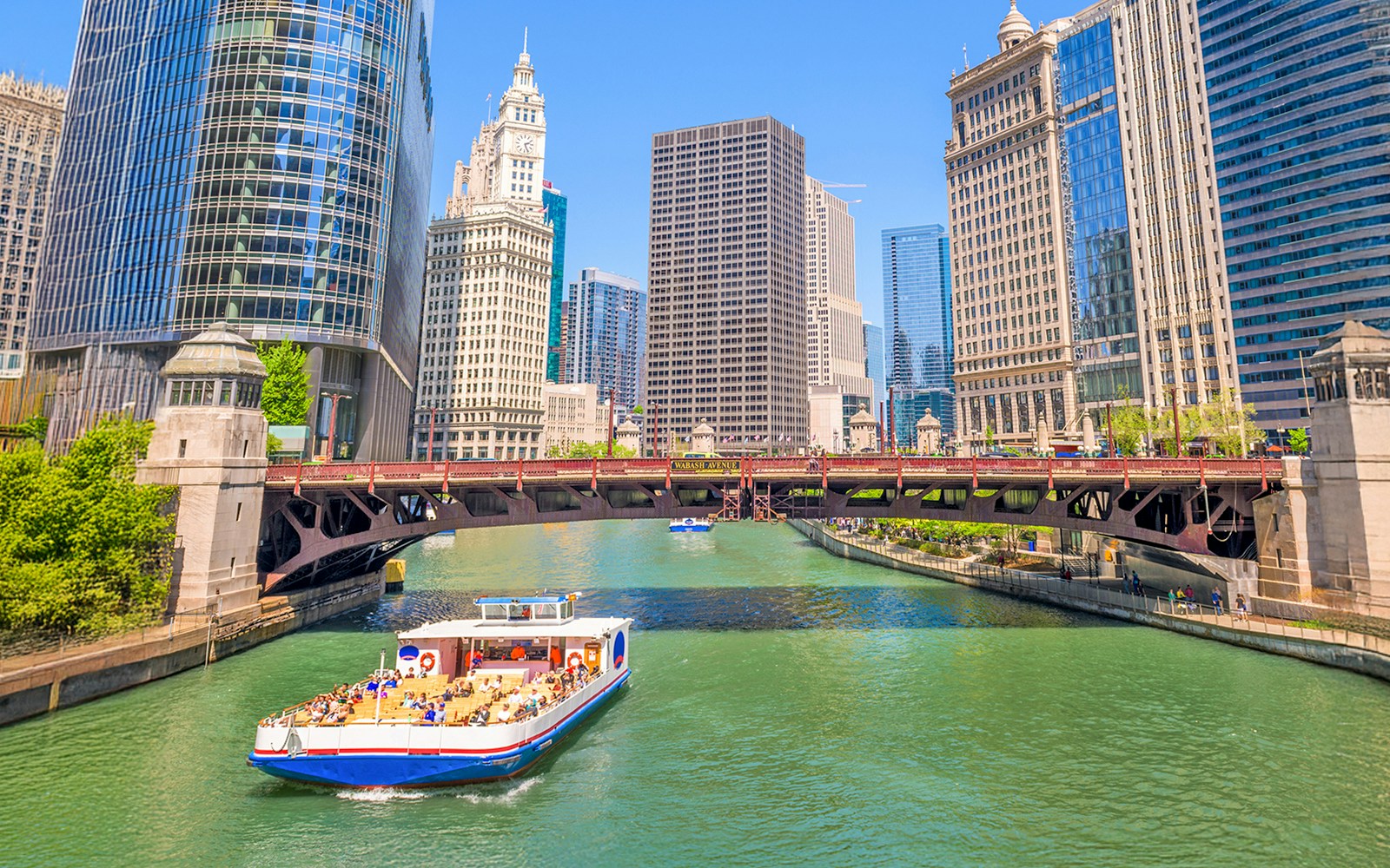 Chicago River cruise boat passing under a bridge with city skyscrapers in the background.