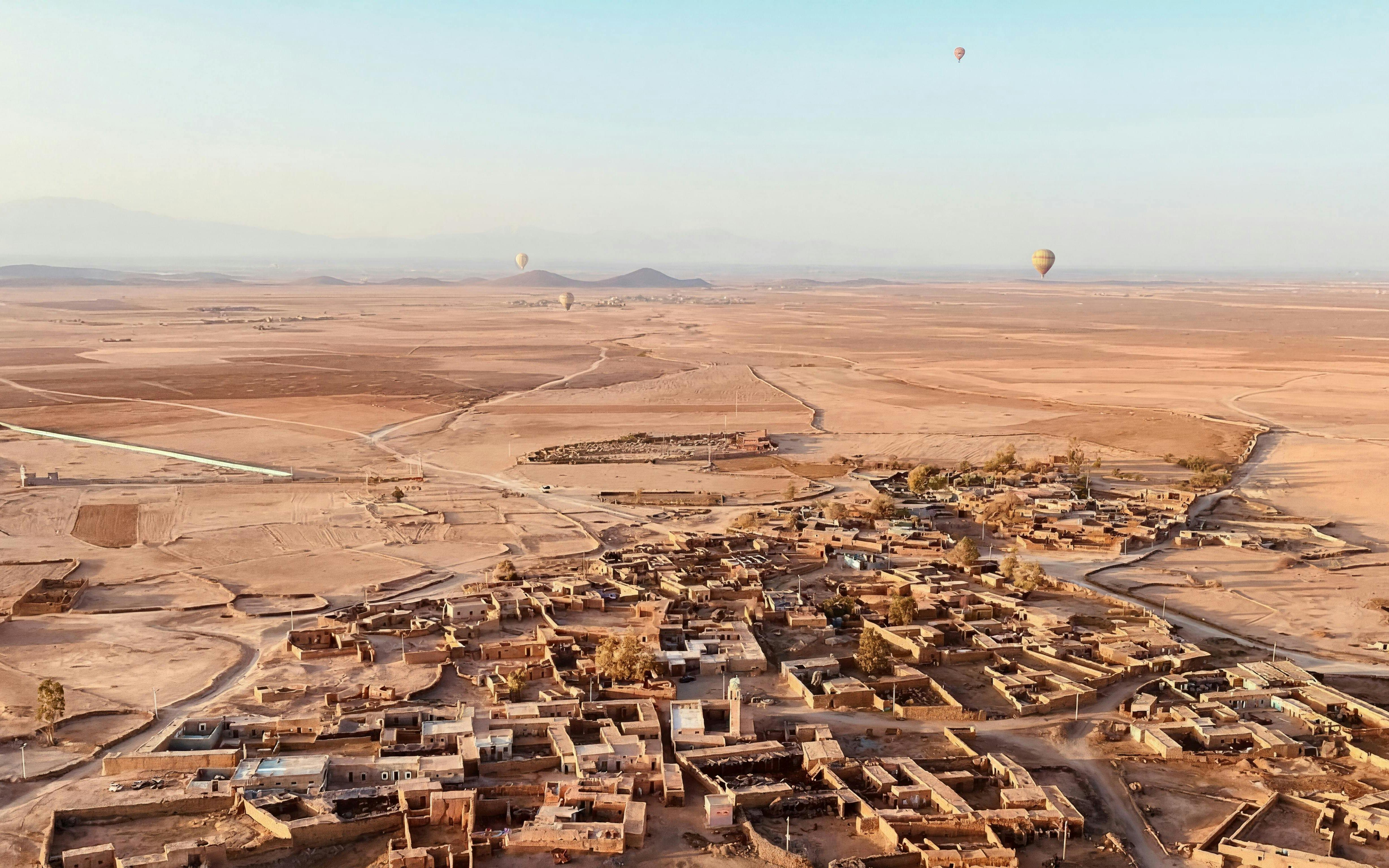 Hot air balloons over Marrakech desert landscape at sunrise, with Berber village below.