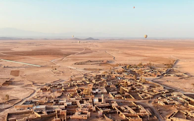 Hot air balloons over Marrakech desert landscape at sunrise, with Berber village below.