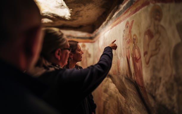 Visitors examining frescoes in the Roman Catacombs during a guided tour.