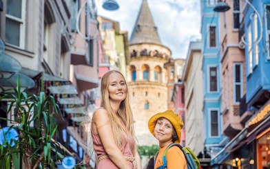 Visitors in front of Galata Tower, Istanbul, with colorful buildings nearby.