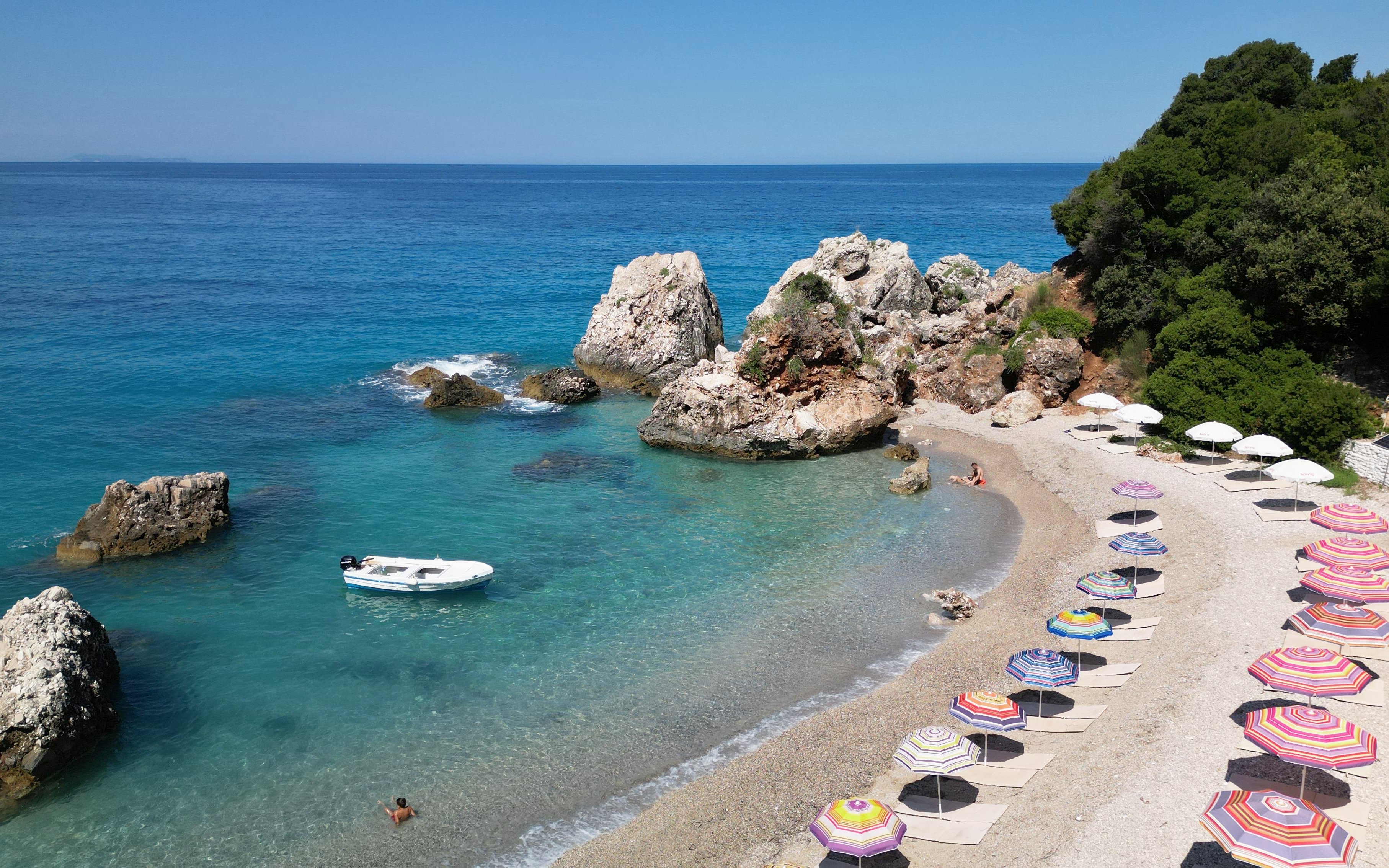 Krorëz Bay beach with colorful umbrellas and rocky shoreline, Albanian Riviera.