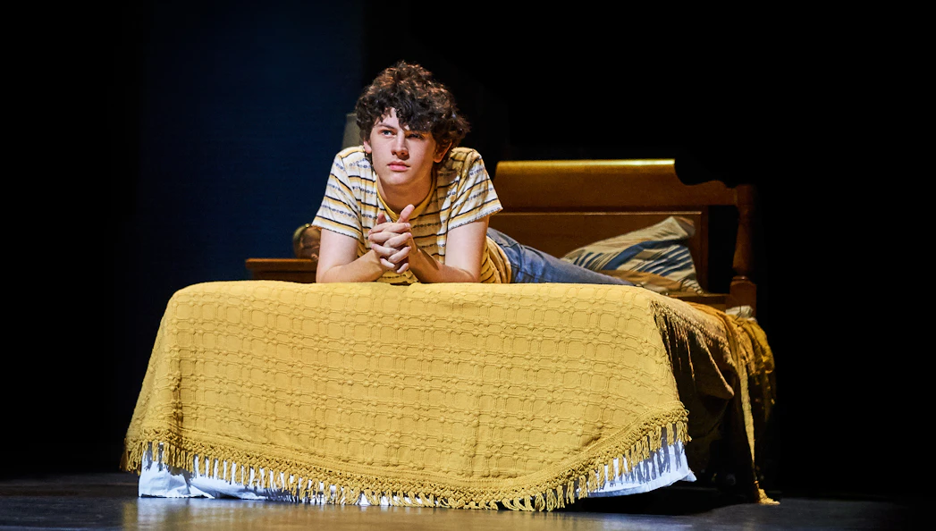 Young person lying on a bed, scene from "Almost Famous" stage production.
