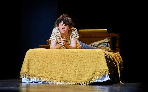 Young person lying on a bed, scene from "Almost Famous" stage production.