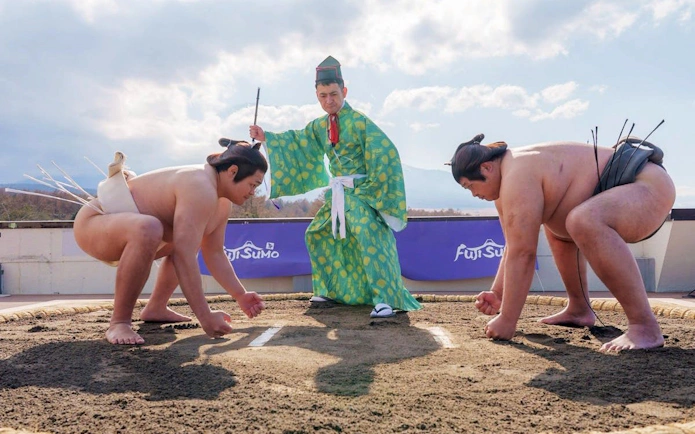Sumo wrestlers face off with a referee in traditional attire at Yamanashi Fuji Sumo Show.