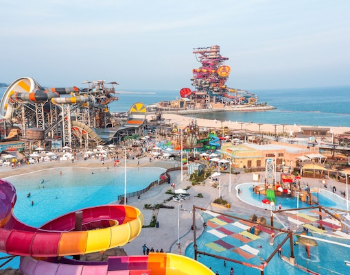 Aerial view of colorful water slides and pools at Meryal Waterpark by the sea.