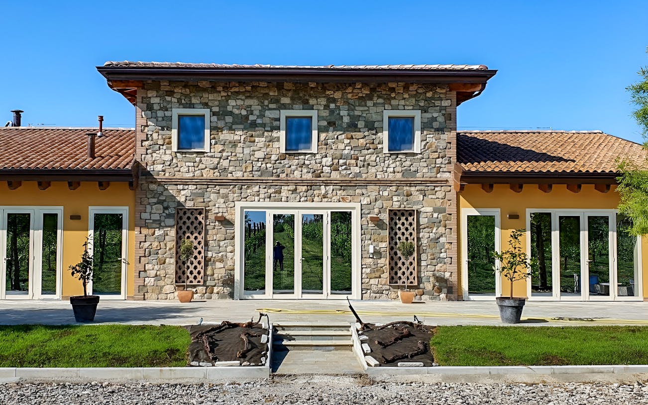 Stone building at Acetaia La Vedetta in Modena, Italy, with vineyard reflection in windows.