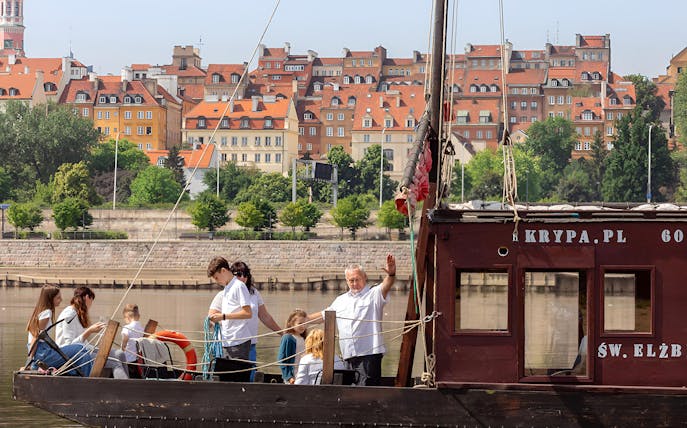 Traditional Galar cruise on the Vistula River with passengers, Warsaw's Old Town in the background.
