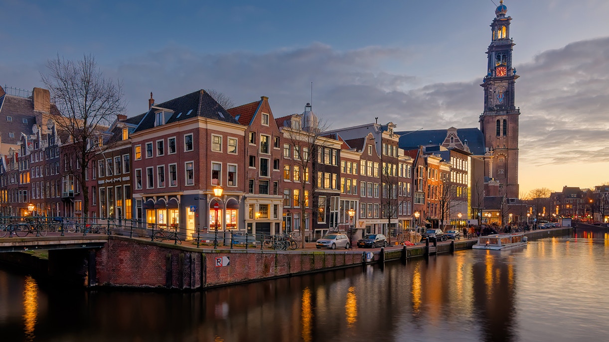 Anne Frank House and Westerkerk tower along Amsterdam canal at dusk.