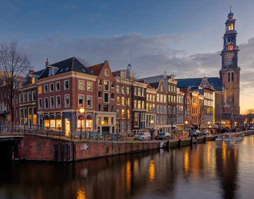 Anne Frank House and Westerkerk tower along Amsterdam canal at dusk.