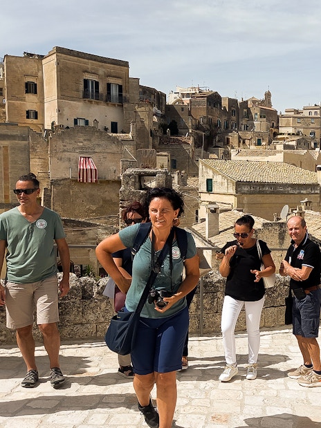 Tourists exploring Matera with audio guide, historic cave houses in background.