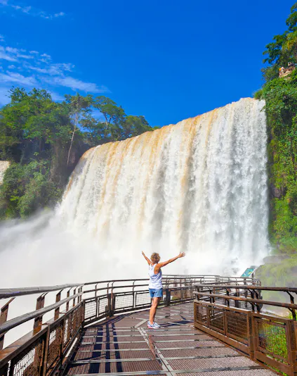 Visitor on walkway admiring Iguazu Falls, surrounded by lush greenery.