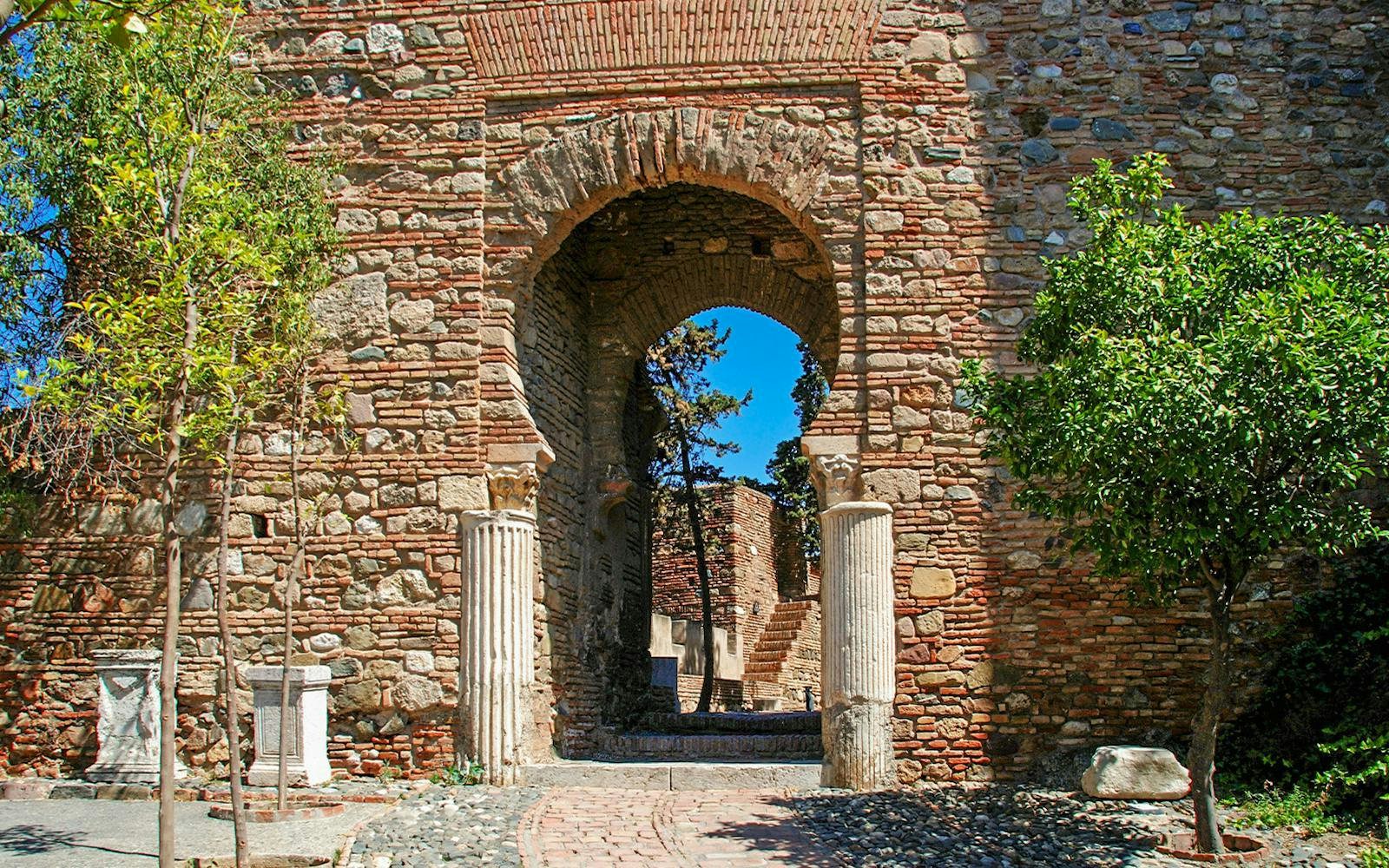Column Gate at Malaga castle with stone archway and trees, Malaga, Spain.