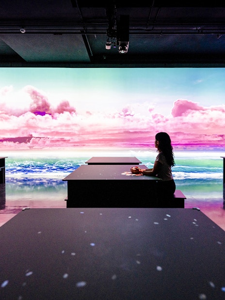 Person seated at ARTE TEA BAR, Arte Museum Dubai, with vibrant digital ocean and sky display.