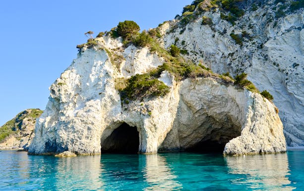 Keri caves on Marathonisi Island, Greece, with clear blue water and rocky cliffs.