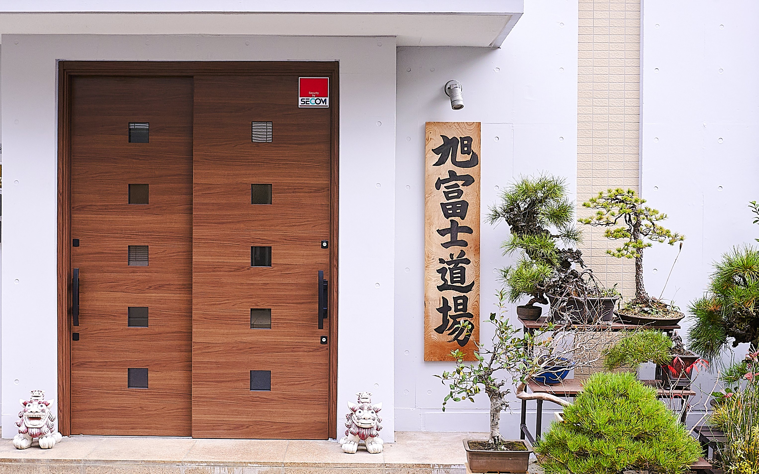 Entrance to sumo dojo in Koto City with bonsai trees and traditional signage.