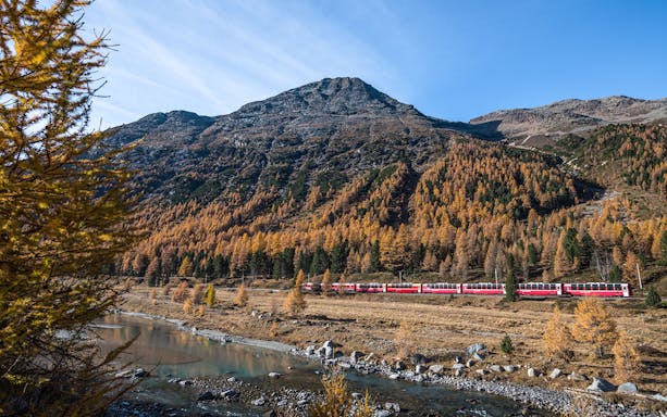 Bernina Express train traveling through autumn landscape between St. Moritz and Tirano.