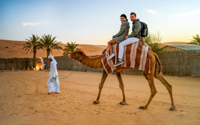Couple on camel during Dubai desert safari with guide leading.