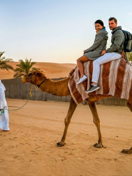 Couple on camel during Dubai desert safari with guide leading.