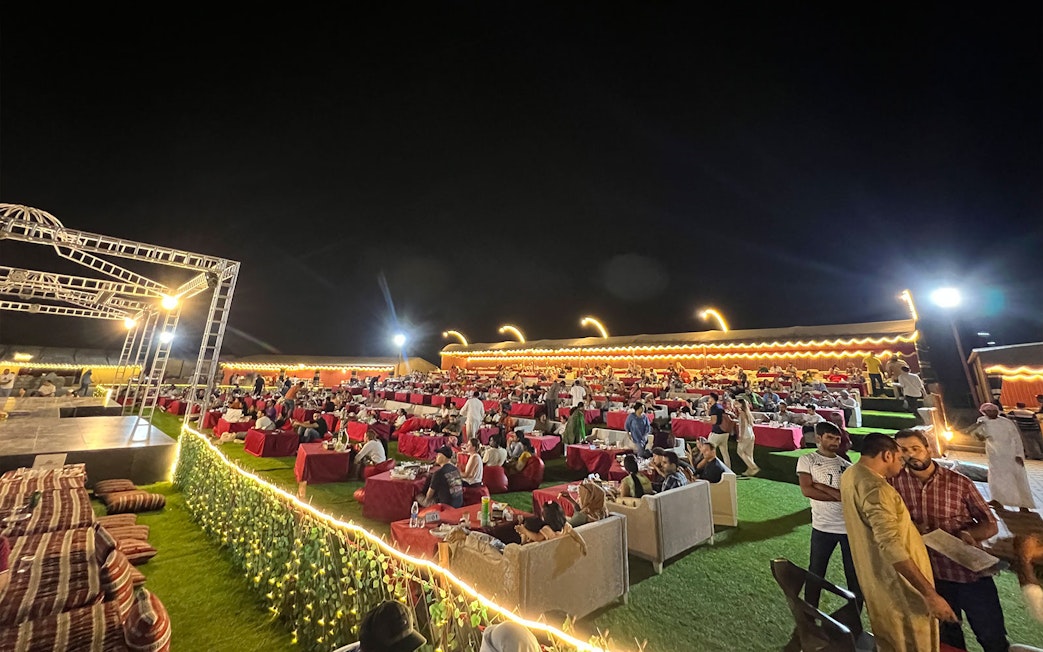 Outdoor dining setup at a Dubai desert safari with guests enjoying BBQ dinner and live shows.