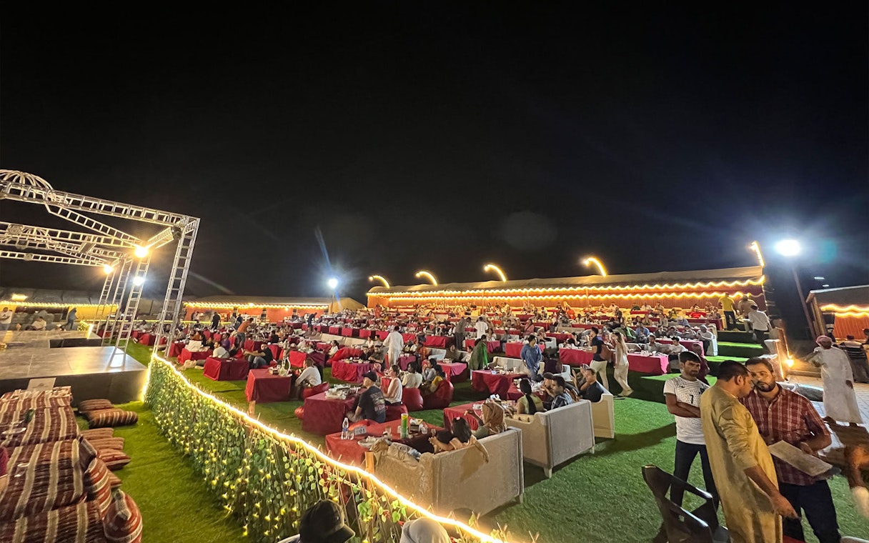 Outdoor dining setup at a Dubai desert safari with guests enjoying BBQ dinner and live shows.