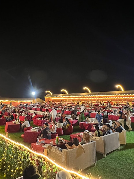 Outdoor dining setup at a Dubai desert safari with guests enjoying BBQ dinner and live shows.