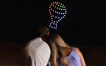 Couple watching drone light show forming hot air balloon shape in Dubai desert.