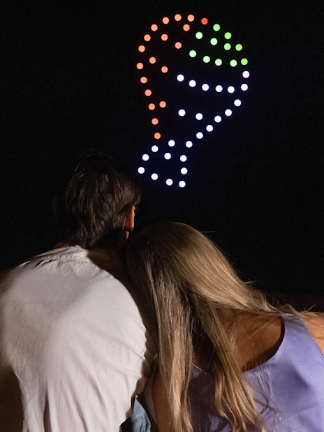 Couple watching drone light show forming hot air balloon shape in Dubai desert.