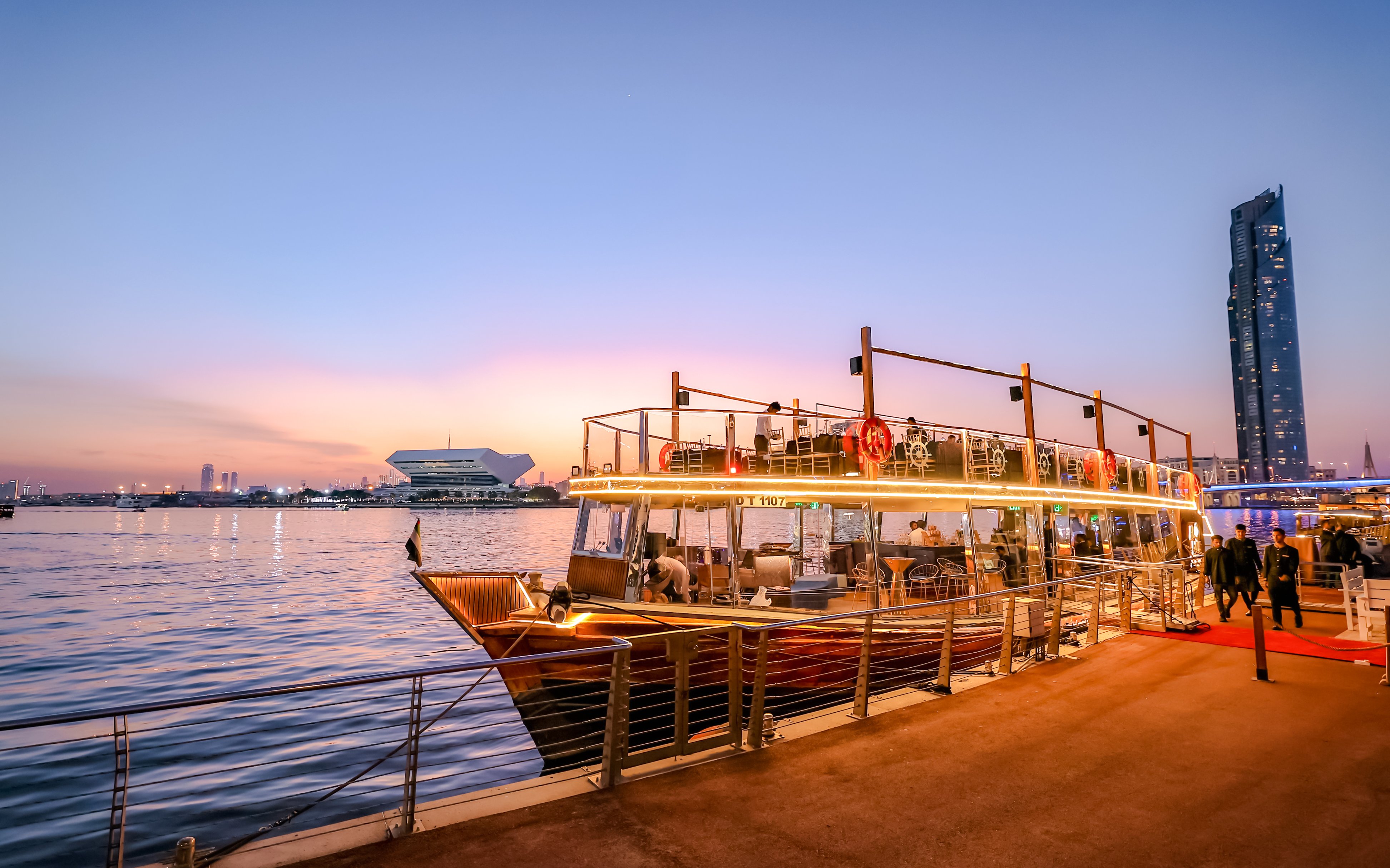 Dubai Canal dinner cruise boat docked at sunset with city skyline.