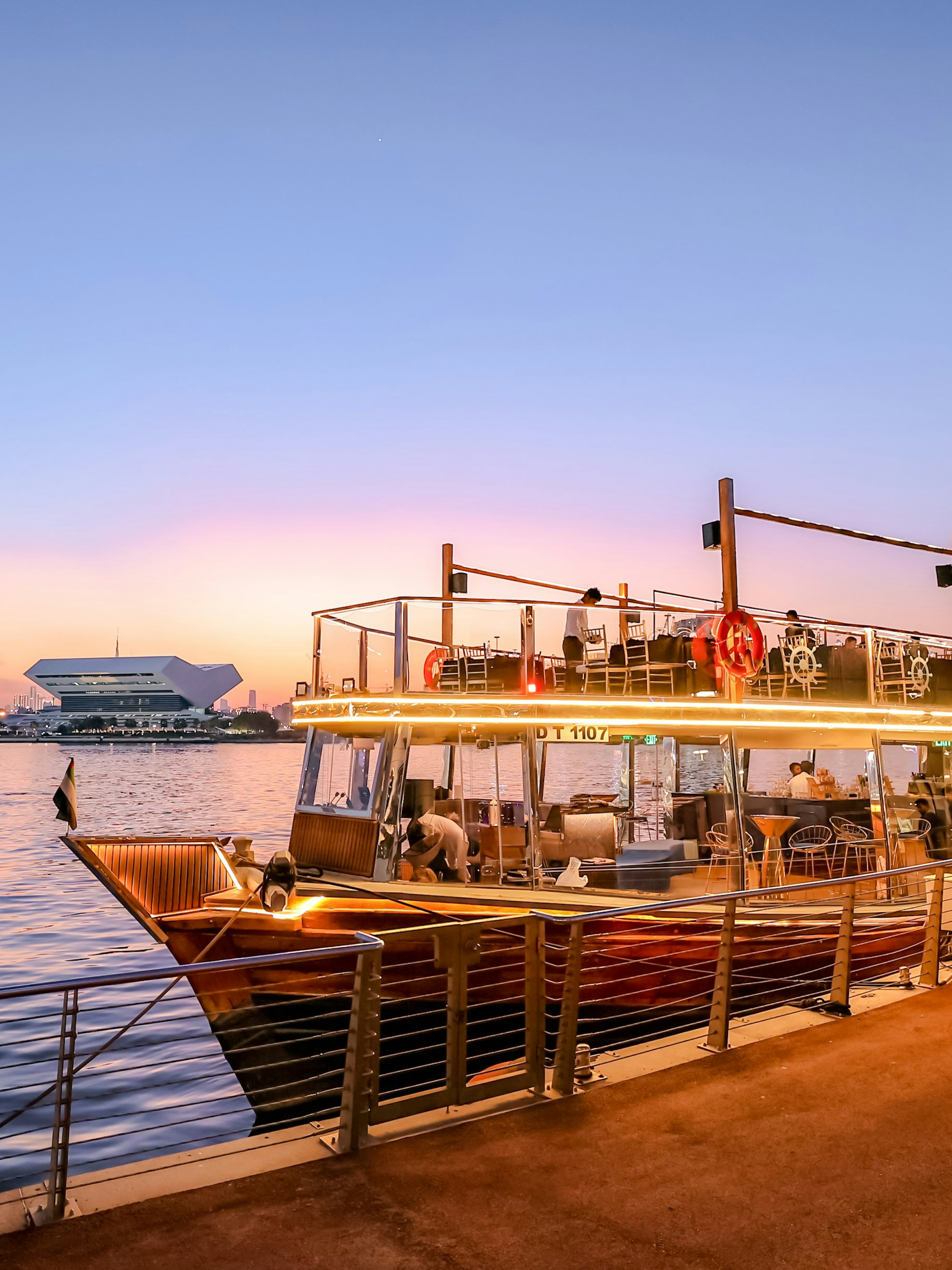 Dubai Canal dinner cruise boat docked at sunset with city skyline.