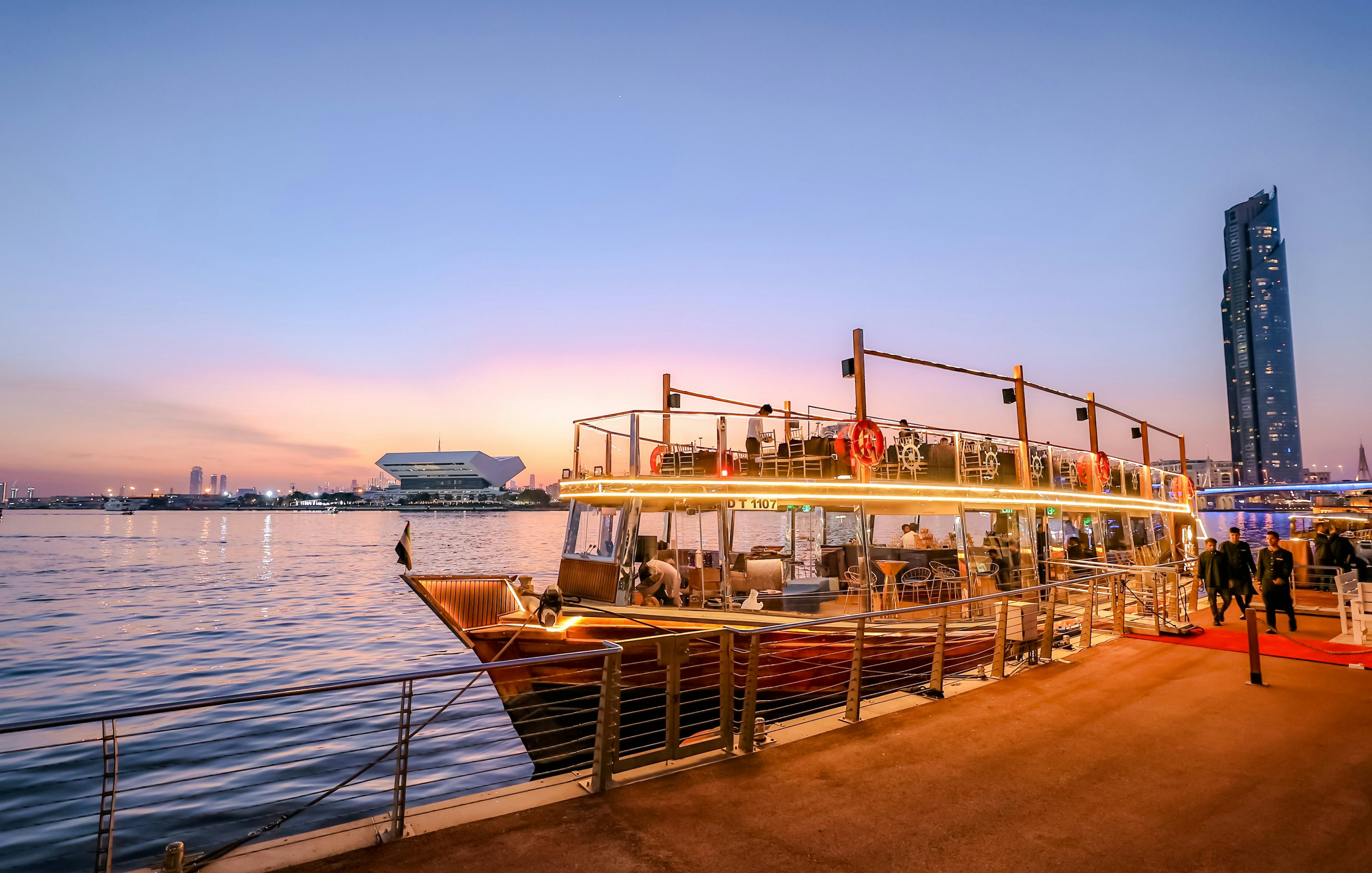 Dubai Canal dinner cruise boat docked at sunset with city skyline.