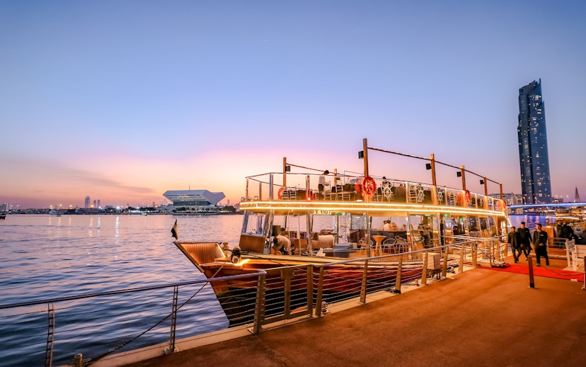 Dubai Canal dinner cruise boat docked at sunset with city skyline.