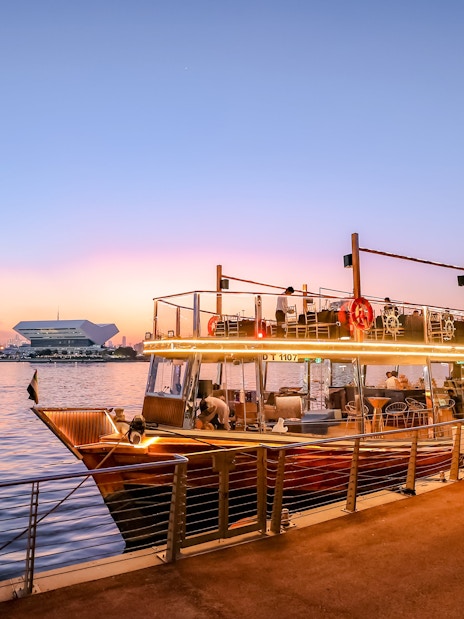 Dubai Canal dinner cruise boat docked at sunset with city skyline.